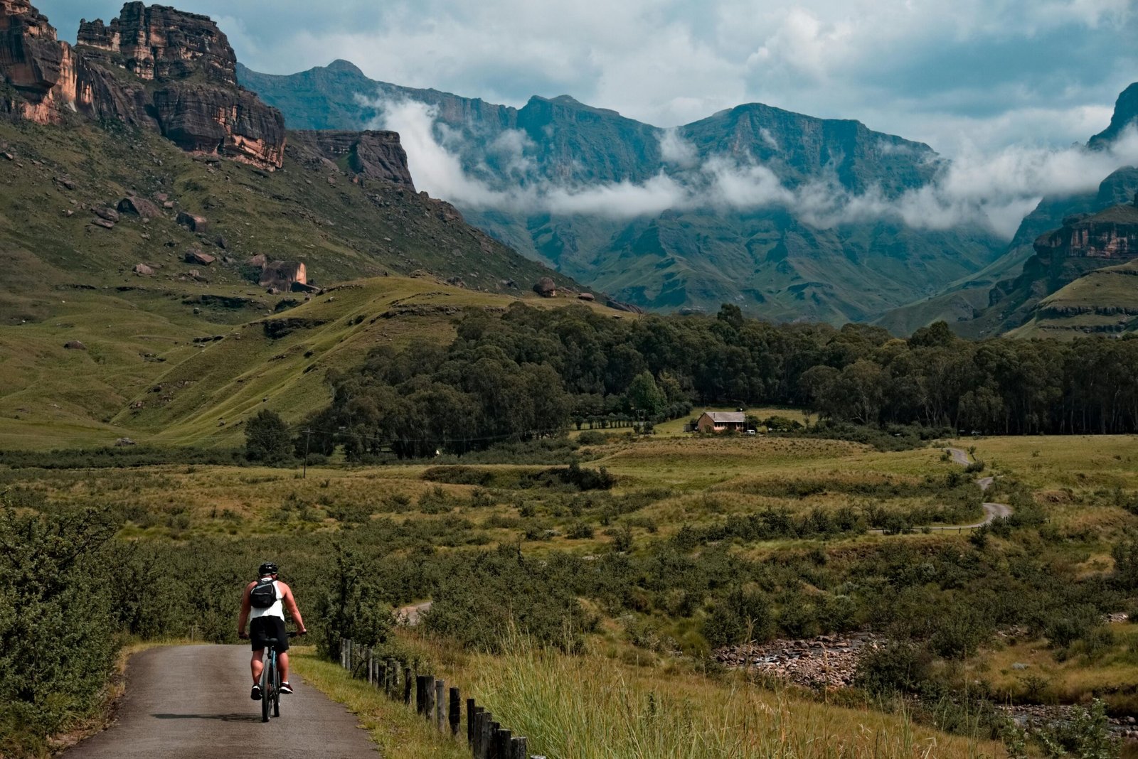 A cyclist rides through a stunning mountain valley under an overcast sky, showcasing a serene landscape.