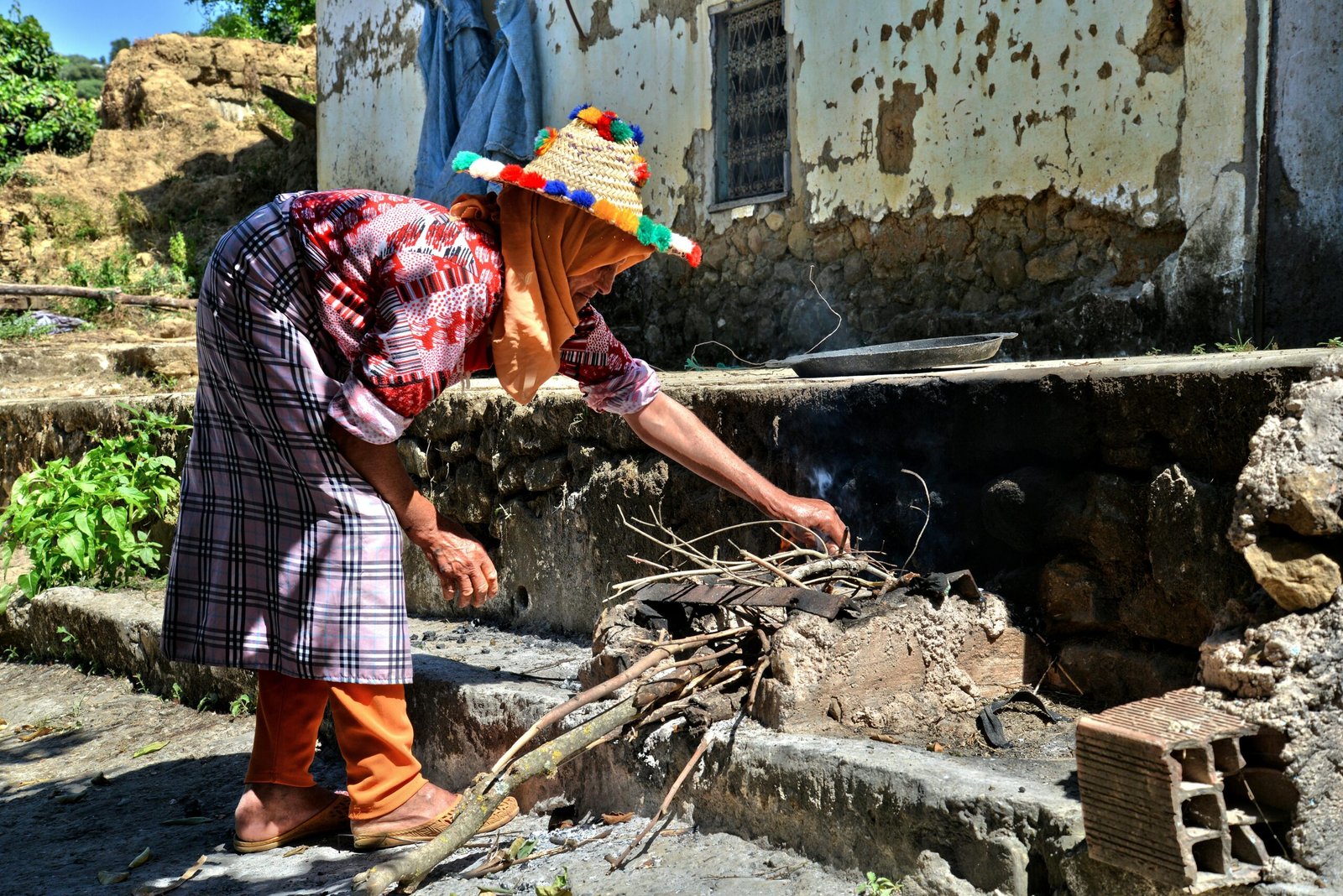 Woman in colorful attire tends to outdoor traditional stove in Taounate, Morocco.