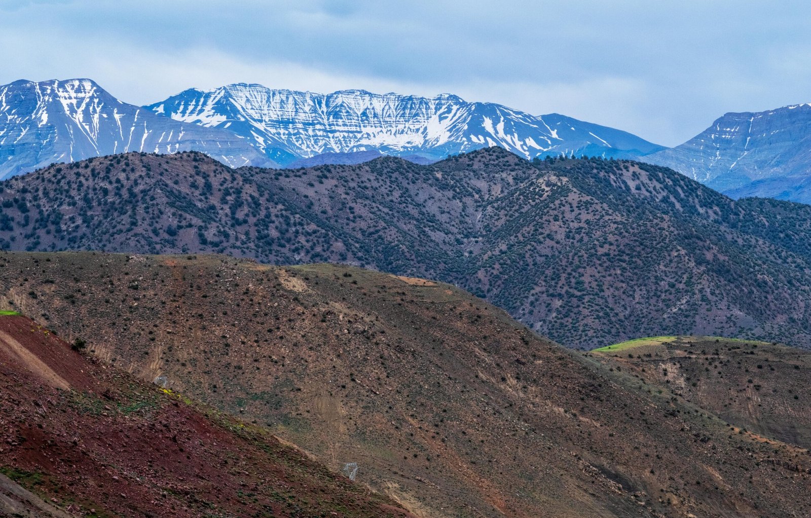 Breathtaking landscape of the Atlas Mountains with snowy peaks and arid foreground in Morocco.